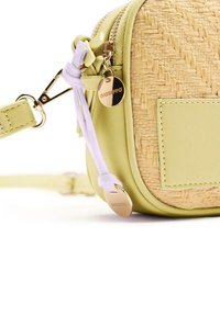 Pequeña bolsa cruzada con textura de paja tejido en color beige, imitación de cuero verde suave, herrajes dorados y un charm decorativo.