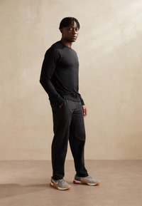 Svart långärmad skjorta med texturerad tyg, kombinerad med svarta byxor och grå sneakers med röda accenter och ett nätmönster.