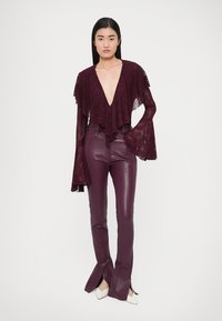 Karmínový čipkovaný top s vrstvenými rukávmi, v kombinácii s karmínovými koženými nohavicami s vysokým pásom a bočnými rozparkami, doplnené bielymi špicatými podpätkami.