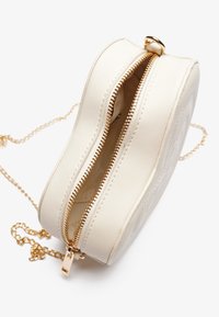 Okrągła torebka na ramię w kolorze kremowym, wykonana ze sztucznej skóry, z złotym suwakiem i łańcuszkiem na pasku. Widoczny fakturowany wzór.