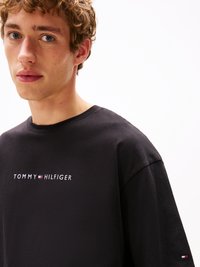T-shirt noir en coton présentant le logo "TOMMY HILFIGER" en blanc avec des accents rouges et bleus ; coupe décontractée et design à col rond.
