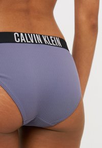 Ribane boksar Calvin Klein v potlačenem sivem lila odtenku z črnim pasom, ki vsebuje belo logotipno besedilo. Gladka tekstura in prilega zasnova.