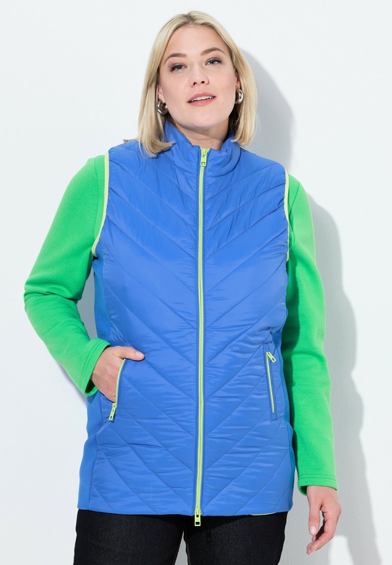 Vadderad blå väst med gröna långärmade ärmar och dragkedjefickor, med ståkrage och kontrasterande neon-dragkedjor.