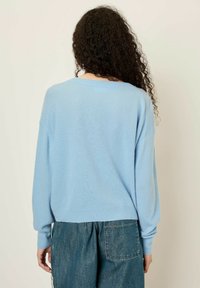 Pull en tricot lâche bleu clair, avec un large col et des poignets côtelés. Texture douce avec des manches longues et une coupe légèrement cropped.