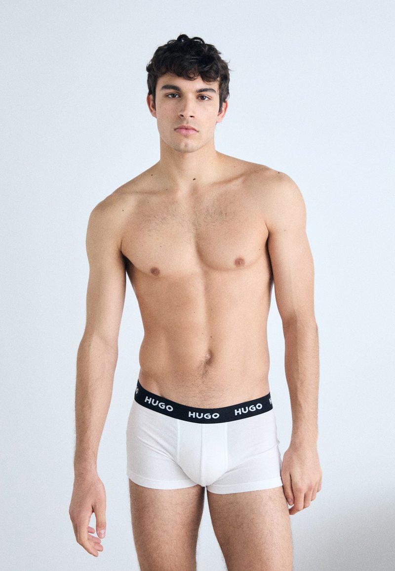 Weiße Boxer-Briefs mit einem schwarzen elastischen Bund, der mit "HUGO" beschriftet ist. Der Stoff wirkt glatt und enganliegend, ohne sichtbare Muster oder zusätzliche Akzente.