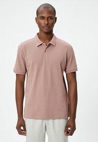 Helles rosa Poloshirt aus Strickstoff mit geripptem Kragen und kurzen Ärmeln. Zwei Knöpfe am Hals und strukturierte Akzente an den Ärmeln.