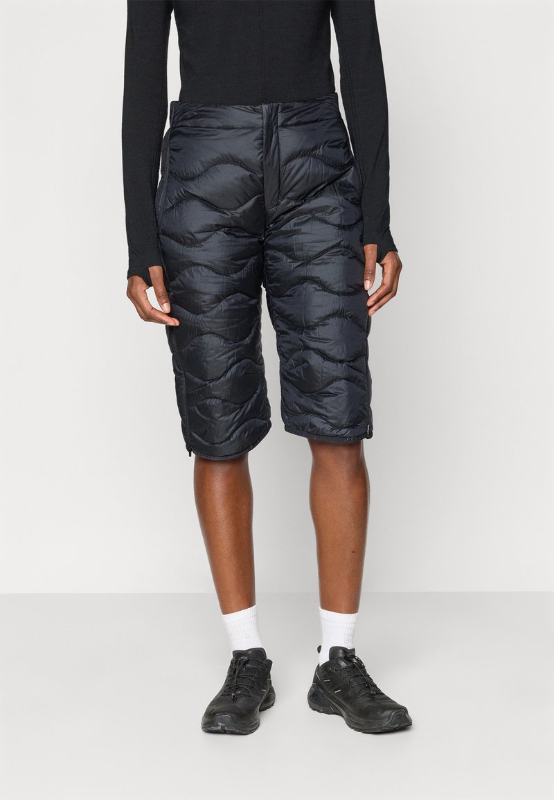 Calções pretos acolchoados com um design acolchoado, apresentando uma cintura alta e fecho frontal. Usados com sapatos pretos e meias brancas.