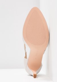 Escarpin beige pour femme à bout pointu avec semelle texturée et bride, présenté en position verticale sur fond blanc.