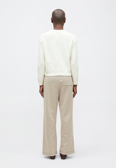 Biała sweter z teksturowanego materiału, ozdobiony wzorem w romby, w połączeniu z beżowymi spodniami o szerokich nogawkach, widok z tyłu. Prosty design, bez widocznych logo.