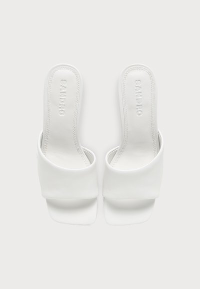 Paire de sandales blanches ouvertes à l'avant avec larges brides et "SANDRO" embossé sur les semelles intérieures, vues de dessus sur un fond clair.