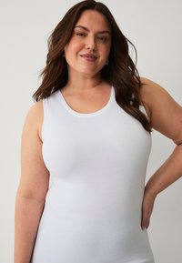 Weißes Tanktop aus glattem Baumwollstoff mit Rundhalsausschnitt und weiten Armausschnitten. Einfaches, figurbetontes Design ohne sichtbare Muster oder Akzente.