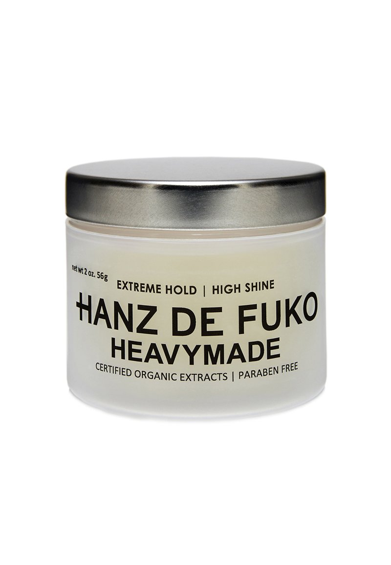 Bocal translucide avec un couvercle en métal argenté, étiqueté "Hanz de Fuko Heavymade" en lettres noires en gras. Contient 2 oz de produit de coiffage.