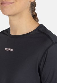 Černé sportovní tričko s technologií odvádění vlhkosti, kulatým výstřihem a krátkými rukávy. Na hrudi je růžové logo "ROSSIGNOL" a má ploché švy.