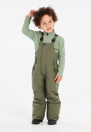 Salopette verde con bretelle regolabili e tasche con zip, abbinata a un top in pile verde chiaro; entrambi sono caldi e imbottiti.