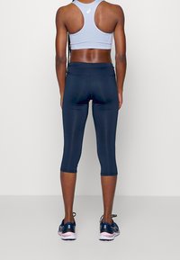 Leggings capri blu navy e reggiseno sportivo azzurro, realizzati in tessuto elasticizzato. Design con spalline sulla schiena, abbinati a scarpe da ginnastica scure.