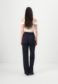 Marineblå bredbuks med elastisk linning, kombinert med en hvit off-the-shoulder topp. Glatt stoff og minimalistisk design.