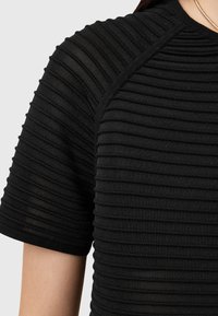 Zwarte geribbelde t-shirt met textuur van verticale lijnen, korte mouwen en een ronde halslijn, gemaakt van een zachte, rekbare stof.