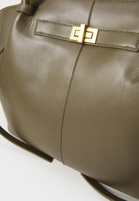 Oliivinvihreä nahkainen käsilaukku, jossa on sileä pinta, kultainen lukko ja saumojen varrella tikattu koristelu.