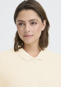 Haut en maille jaune clair avec un motif texturé, doté d'un col classique et de boutons ronds, présenté en portrait en gros plan.