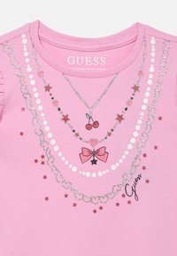 Růžové tričko s krátkými rukávy zdobené třpytivými motivy náhrdelníků, mašlí, třešní a hvězd. Měkká látka s nabráním na rameni.