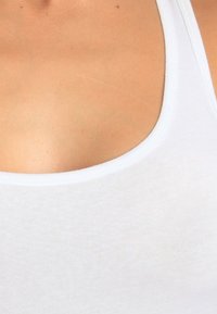 Top in cotone bianco senza maniche con scollatura arrotondata, caratterizzato da una texture morbida e cuciture minime, progettato per comfort e facilità di movimento.