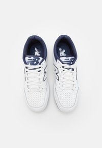 Białe sneakersy z granatowymi akcentami, perforowane detale na czubku, płaskie sznurówki oraz duże logo "NB" po boku i na języku.
