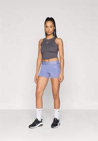 Pilkas sportinis trumpas marškinėlis, mėlyni Nike Pro šortai su logo, derinami su juodais sportiniais batais ir baltais kulkšninių kojinėmis su logo.