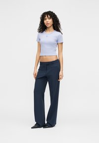 Lichtpaarse cropped t-shirt met een ronde hals, gecombineerd met donkerblauwe wijde broekspijpen en zwarte puntige platte schoenen.