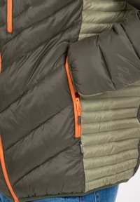 Quilted pufferjakke i mørkegrøn og oliven med orange lynlåse. Den teksturerede stof har diagonale og vandrette syningsmønstre.