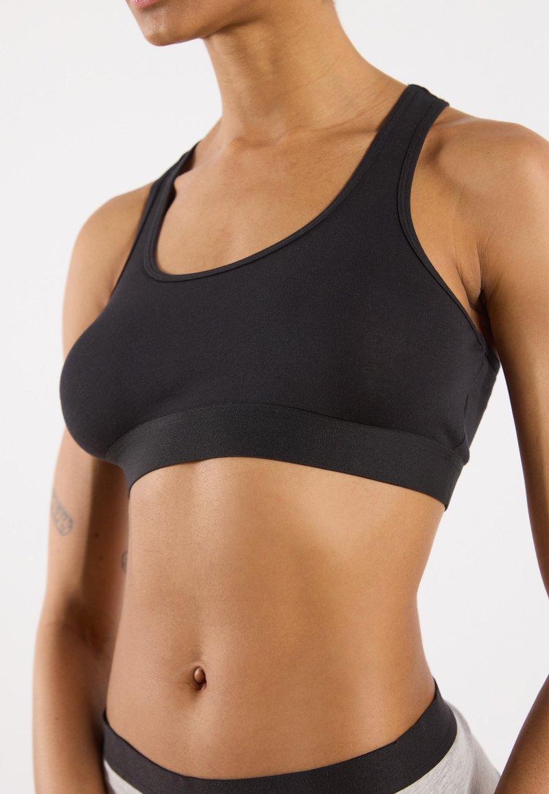 Soutien-gorge de sport noir avec un col arrondi et une large bande élastique en bas. Tissu lisse, ajustement extensible et sans matériel ou bretelles visibles.