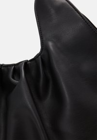 Svart läderväska med en mjuk, samlad textur och en slät yta samt framträdande sömmar längs kanterna.