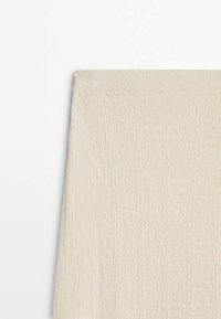 Section de jupe en tissu texturé couleur crème avec une ceinture élastique, présentée sur un fond blanc.