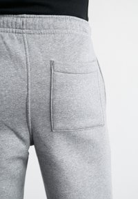 Šedé tepláky vyrobené z měkké tkaniny, s kapsou na zadní straně, elastickým pasem a šitými detaily podél švů.