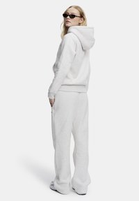 Lys grå hettegenser og matchende joggebukser i myk stoff. Avslappet passform med hette og kengurulomme, brukt med elegante svarte solbriller.