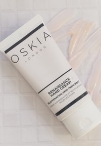 Tubo di crema per le mani OSKIA Renaissance, bianco con testo nero, con cappuccio a scatto e una striscia di crema liscia e chiara accanto ad esso.