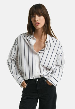 Witte katoenen blouse met marineblauwe verticale strepen, een losse pasvorm, knoopsluiting aan de voorkant, een borstzak en opgerolde mouwen, gecombineerd met zwarte jeans.