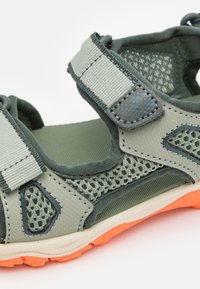 Sportsandaler med en grønn nettingoverdel med grå detaljer, justerbare stropper og en oransje gummisåle med strukturert mønster.