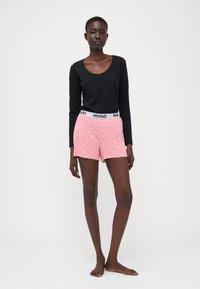 Black long-sleeve top paired with pink shorts featuring a white pattern and black HUGO waistband. Smooth texture, casual fit.