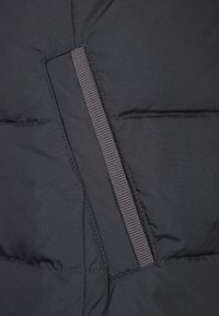 Svart stoppat tyg med en slät textur, med en vertikal dragkedjeficka och subtil sömnad. Elastisk detalj längs dragkedjan.