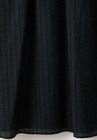 Tissu noir avec des rayures verticales texturées subtiles, suspendu avec de légers plis.