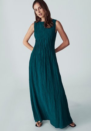 Abito lungo senza maniche di colore verde acqua con un design a pieghe testurizzate. Presenta un collo rotondo e arriva fino a terra, abbinato a sandali neri.