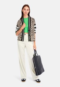 Leopardenmuster-Cardigan mit schwarzem Besatz, lebendiges grünes Cropped-Top, weite weiße Hose und schwarze Tote-Bag mit Reißverschlussdetails und gemusterten Akzenten.