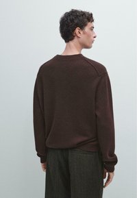 Brązowy sweter z dzianiny, z rękawami raglanowymi, okrągłym dekoltem i miękką fakturą, w połączeniu z ciemnymi, textured spodniami. Widoczne szwy i ściągacze na rękawach.