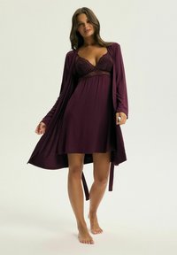 Nocna sukienka w kolorze śliwkowym z koronkowym wykończeniem na bodice i zwiewnym szlafrokiem. Tkanina jest gładka, ma długie rękawy i paskiem w talii.