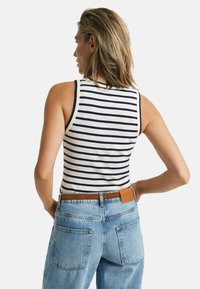 Top sin mangas a rayas en mezcla de algodón blanco y azul marino, combinado con jeans de denim azul claro. Presenta un ajuste casual y un cinturón de cuero marrón.