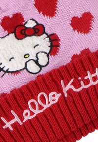 Roze gebreide muts met rode harten, met een fluffy witte kat graphic met een rode strik. De rand heeft "Hello Kitty" in het wit geborduurd.