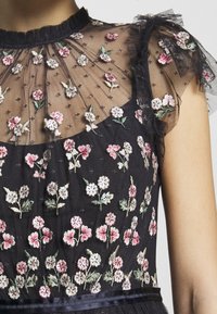 Robe noire avec un bustier en tulle transparent brodé de fleurs et des manches volantées. La broderie comprend des fleurs roses et lilas sur un tissu en tulle.
