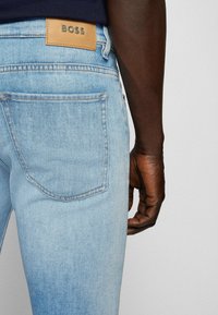 Jeans en denim bleu clair arborant un design classique avec une étiquette en cuir BOSS sur la ceinture et des coutures contrastées sur les poches.
