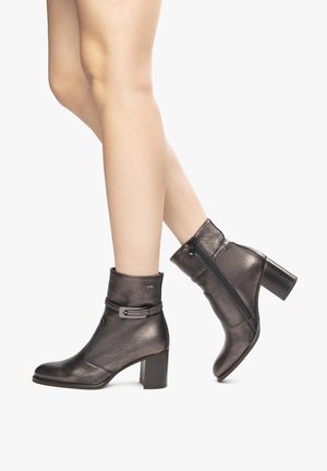 Bottines grises métalliques avec un talon moyen, présentant une sangle enroulante et une fermeture éclair sur le côté, texture lisse avec une silhouette élégante.