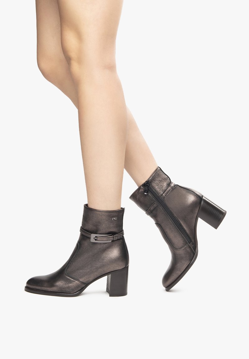 Stivaletti metallici grigi con tacco medio, dotati di fascia avvolgente e zip laterale, texture liscia e silhouette elegante.